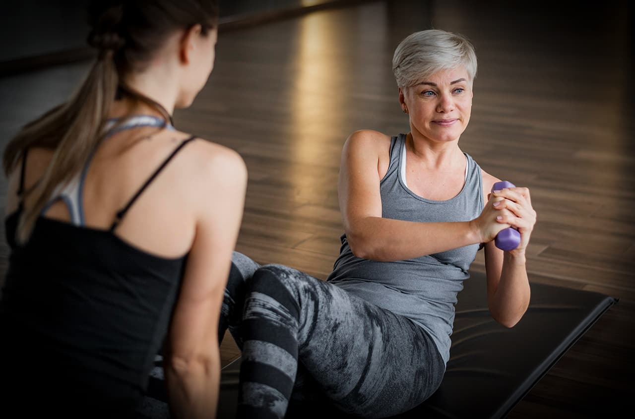 Woman in her forties doing core work with a dumbbell alongside her coach
